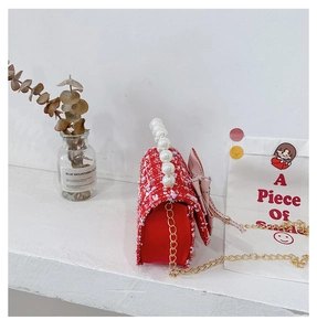 Detail of red tweed girl bag featuring pearl handle, gold chain and bow decoration