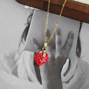 Collier fraise doré minimaliste avec émail rouge et pierres pavées sur magazine de mode