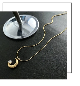 Close-up of polished crescent moon necklace in gold with a small diamond accent