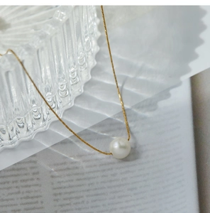 Close-up of a single white pearl on a gold titanium steel chain with a glass backdrop
