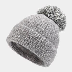 Detail view of winter beanie showing thick knit texture, faux fur pom and satin silk lining