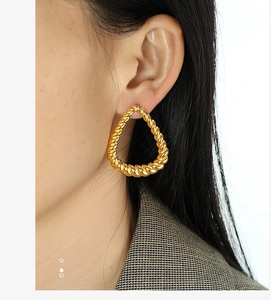 Detail of large gold teardrop earrings with a textured rope twist design on a model