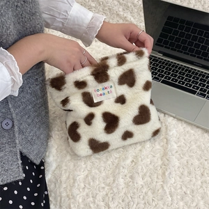Plush makeup bag with brown heart patterns and textile label held in a lifestyle setting