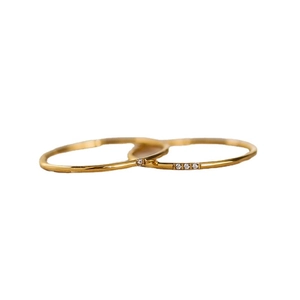 Set of two minimalist gold-plated thin rings with small diamonds on white background
