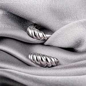 Close-up of silver croissant twist earrings on grey silk fabric showing mirror finish