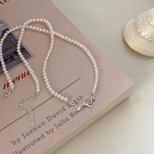 925 silver bow pendant necklace with pearls displayed on a pink book cover