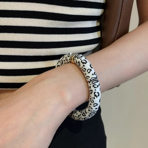 Detail of leopard print bangle with gold metal sphere accent on a female wrist