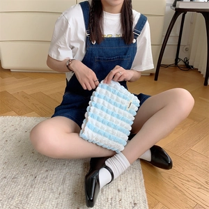 Detail of soft blue and white striped puffy canvas makeup bag held in a cozy home setting