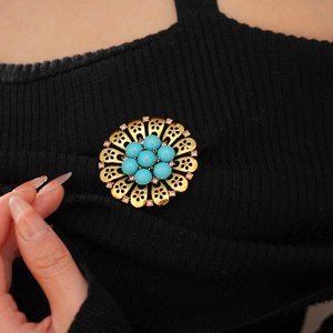 Close-up of vintage gold hollow flower brooch with blue beads on black knitwear
