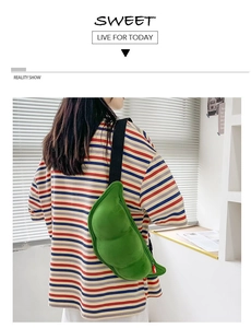 Green plush pea pod crossbody bag shown on a model in a casual indoor setting