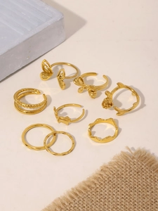 7-piece gold ring set featuring butterfly and rose designs on a textured beige surface