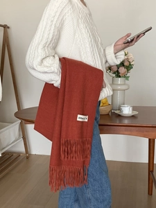 Detailed view of red fringe scarf with different label held by person in white sweater