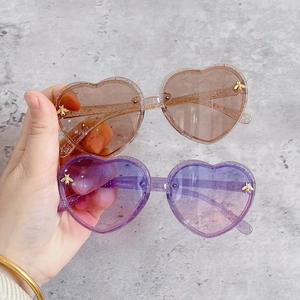 Detail of glittery heart-shaped kids sunglasses with gold bee accents and gradient lenses