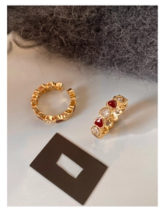 Close-up of gold heart ear cuffs with red enamel and sparkling zircons on plush fabric