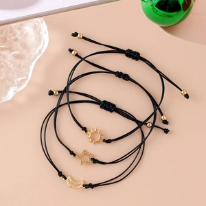 Close-up of black braided sun, moon and star bracelets with gold pendants on warm pink