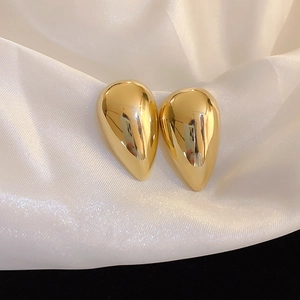 Detail view of high-shine gold teardrop earrings resting on white satin fabric