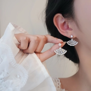 Detail of fan-shaped silver earrings with micro-set zircon stones on model's hand