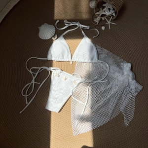 Flat lay of white three-piece bikini with mesh sarong and authentic shell charms