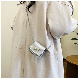 Close-up of a silver chain bag with a decorative metal butterfly buckle worn with a coat