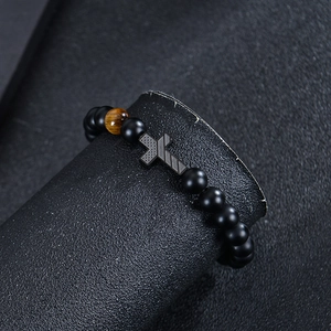 Detail of matte black beads and tiger eye stone bracelet with textured cross charm