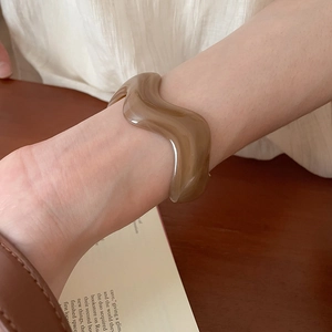 Close-up of translucent amber brown wavy resin bangle on a wrist in warm lighting