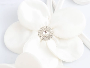 Detail of a white satin 3D flower with sparkling rhinestone center on a camisole top
