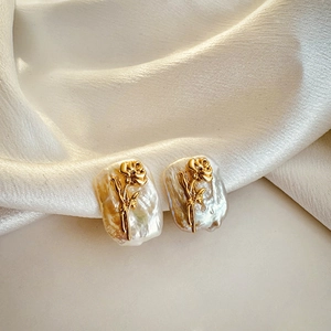 Detailed close-up of golden floral earrings with baroque pearls on soft beige silk