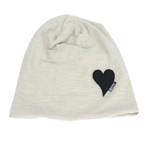 Detail of beige knitted beanie featuring black heart patch and texture weave