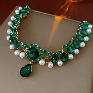 Detailed close-up of a vintage gold necklace with green gemstones and white pearls