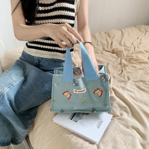 Blue corduroy tote bag with orange butterfly embroidery on top of an art book