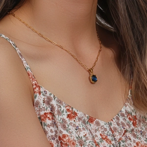 Detail of a paperclip chain necklace with a blue oval zircon pendant on a model