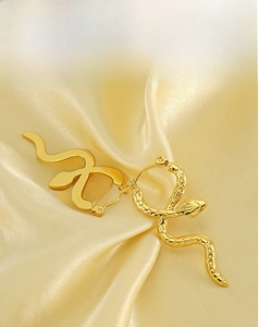 Detail of snake-shaped 18k gold-plated earrings with smooth and scaled texture on silk