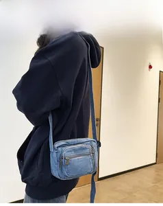 Blue washed denim crossbody bag side view showing multi-zipper compartments on 165cm model
