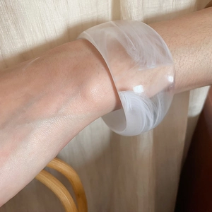 Detail of translucent resin cuff bracelet featuring white smoky texture on a female wrist