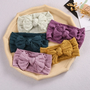 Detail showing five colorful velvet scalloped bow headbands for baby girls in a beige tray