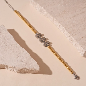 Détail d'un bracelet en perles dorées avec trèfles argentés sur un support en pierre brute