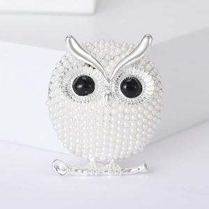 Macro detail of silver owl brooch with white pearls and black bead eyes on white background
