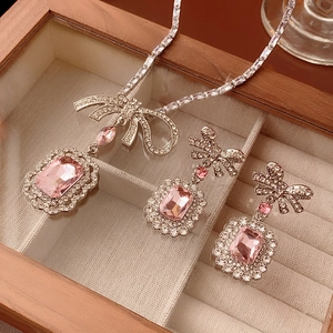 Détail d'un collier à nœud argenté et de boucles d'oreilles rose dans un coffret en bois
