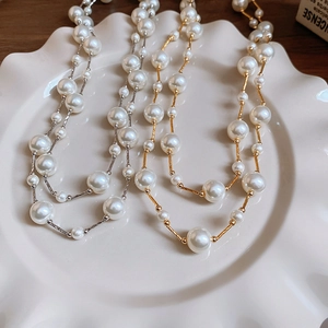 Detail of gradient pearl necklaces with gold and silver chains on a white textured plate