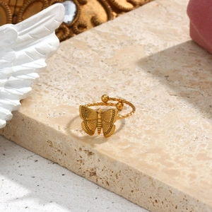 Detailed view of an 18K gold plated butterfly ring on a beige stone surface