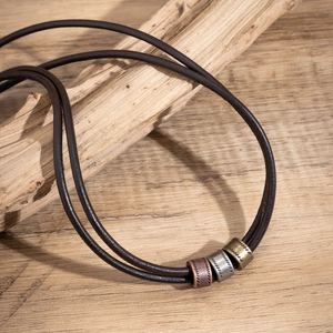 Detailed view of leather cord necklace with bronze silver and gold rings on rustic wood
