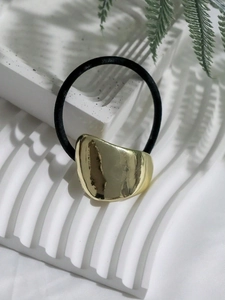 Detailed view of an irregular gold metal piece on a black elastic ponytail holder