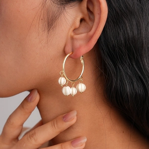 Elegant gold hoop earrings with white pumpkin pendants and tassels on a model