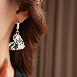 Close-up of a silver-toned hammered heart C-shaped earring worn on a model's ear