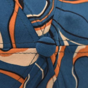 Top detail view of tie-dye baseball cap featuring blue and orange abstract flowing patterns