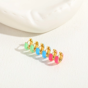 Three pairs of colorful enamel gold-plated hoop earrings on a ceramic display