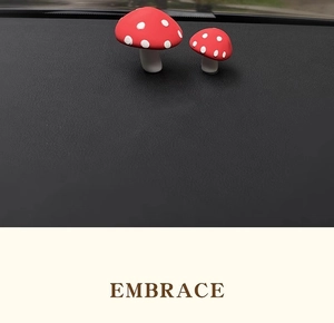 Close-up of two red mushroom car ornaments placed on a black dashboard for decoration