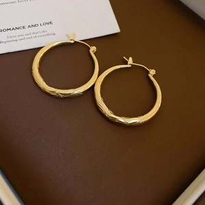 Close-up of golden hoop earrings featuring a vintage textured diamond pattern on leather