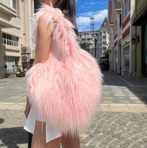 Detail of pink faux fur heart-shaped crossbody bag with long fluffy texture on street