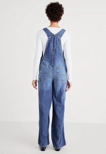 Rear view of loose fit denim dungarees showing cross back straps and large back pockets